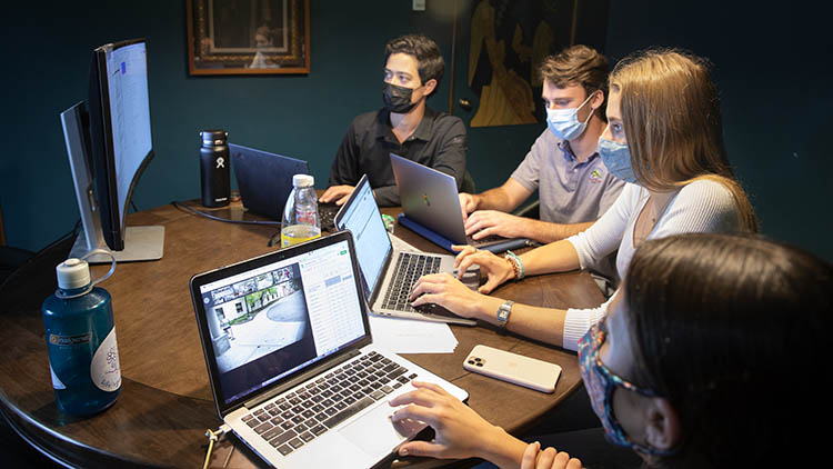 Four students with laptops looking at a central monitor